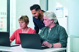 Unterrichtssituation: Kursleitung erklärt Teilnehmenden etwas am Laptop